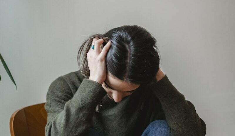 Anxious young woman cover wing ears with hands sitting on chair